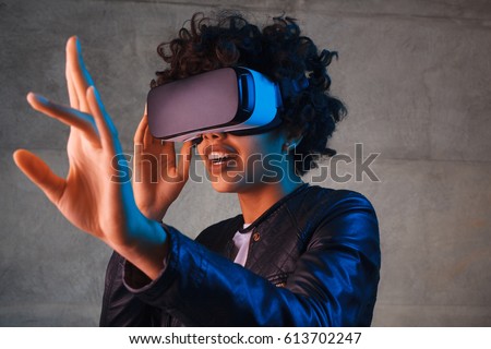 Amazed young woman touching the air during the VR experience. Horizontal studio shot. Royalty-Free Stock Photo #613702247