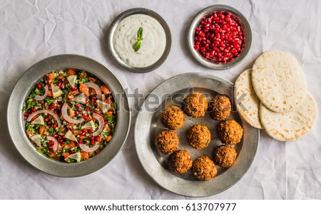 Crispy falafel, Arab pita bread, tabbouleh salad, with pomegranate seeds and white sour cream sauce against white background. Selective focus.