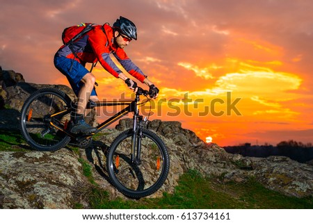 Cyclist Riding the Mountain Bike Down Spring Rocky Hill at Beautiful Sunset. Extreme Sports and Adventure Concept.