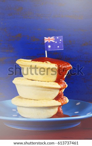 Australian party food with iconic meat pies and tomato sauce on dark red and blue vintage rustic recycled wood background, with applied retro vintage style filters.