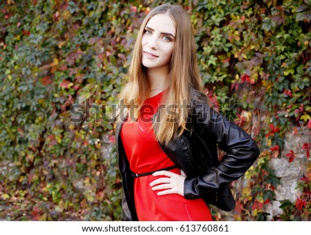 Beautiful young girl in red dress and leather black jacket posing outdoors. Lifestyle, fashion, image for the magazine