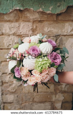 An unusual bouquet of rose flowers and marshmallows in hand against old brick wall