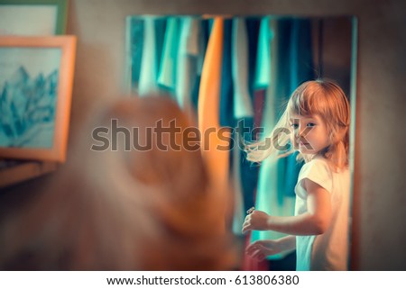 Cute little blonde girl with big eyes is dolling up in front of the mirror. Image with selective focus and toning