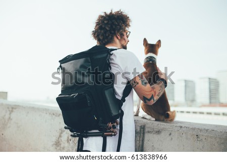 Young trendy hipster with tattoos crazy curly hair with his best friend a little cut basenji puppy rest after a workout on the bridge looking at barcelona Royalty-Free Stock Photo #613838966