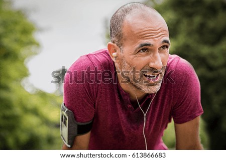 Portrait of athletic mature man after run. Handsome senior man resting after jog at the park on a sunny day. Sweaty multiethnic man listening to music while jogging. Royalty-Free Stock Photo #613866683