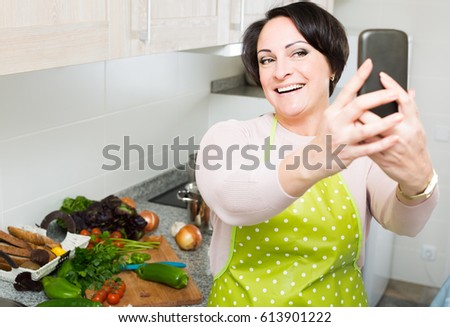 Portrait of smiling american  housewife in apron making selfie in domestic kitchen