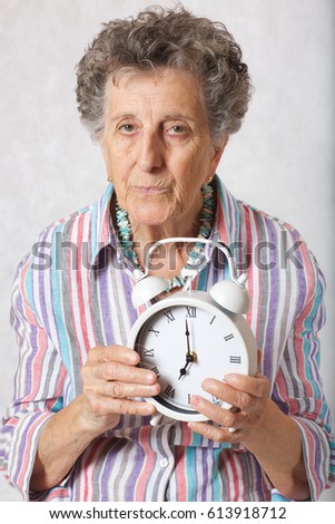 Senior woman between 70 and 80 years old shows vintage alarm clock