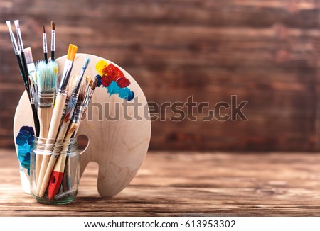 Wooden art palette with tubes of oil paints and a brush. Art and craft tools. Artist's brush, canvas, palette knife. Space for text. Items for children's creativity.Acrylic paint and brushes Royalty-Free Stock Photo #613953302