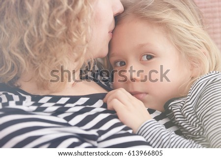 Young mom kissing her little daughter on her forehead