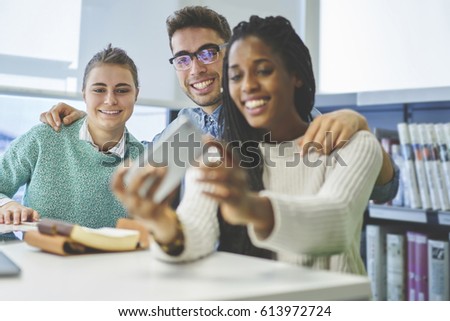 Cheerful young male and female students making photo via smartphone sitting in university library working together on project,colleagues in good mood enjoying break in coworking office taking picture 