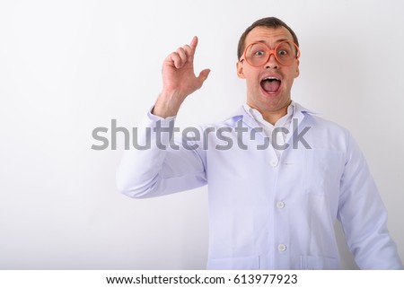 Studio shot of young muscular man doctor looking shocked while pointing finger up and wearing eyeglasses against white background