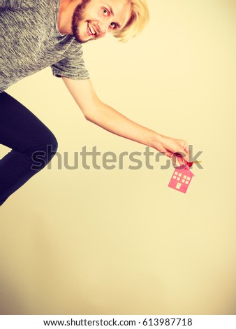 Household savings, housekeeping real estate concept. Running happy man holding keys with small pendant in the shape of a house, studio shot on light background
