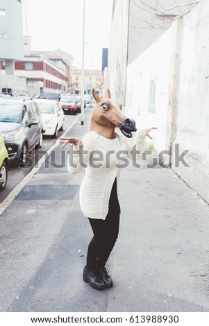 Woman wearing horse mask dancing outdoor in the city - strange, absurd, carnival concept