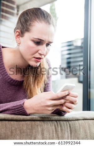 suspicious beautiful young woman frowning in reading and questioning her text messages on her smartphone, patio background, low angle view