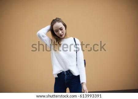 Half length portrait of stylish hipster girl with trendy rucksack and white cotton sweatshirt standing on promotional background. Good looking gorgeous woman with blond hair wear casual brand outfit 