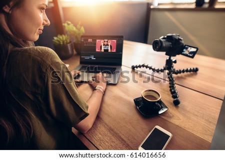 Young woman looking at camera while working on laptop. Young photographer with her camera and laptop on her desk.