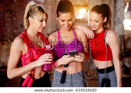 Beautiful young women listening music fitness training workout. Group of attractive females looking at smart phone smiling..
