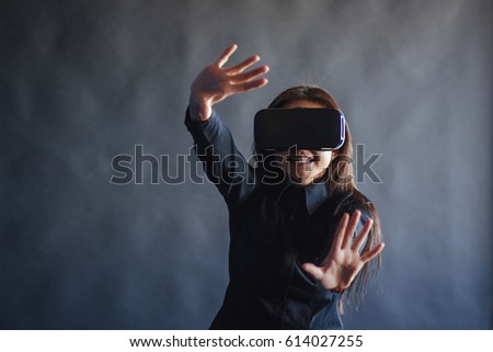 Happy woman on a black background in the studio gets the experience of using VR-glasses virtual reality headset