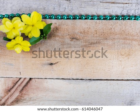 Three yellow flowers and green necklace on a old rough wooden boards background mock up wallpaper surface