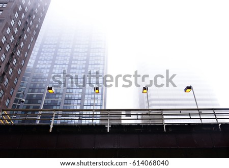 A landscape photograph skyline buildings covered in the misty fog. The view of the photo is from the ground and looking up at a train station stop.