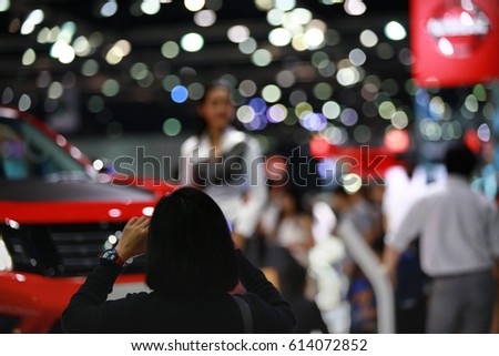 A woman take a photo of pretty and new vehicle by her mobile phone , Visitor shoot a picture in Bangkok motor show even in Thailand, Blurred defocused background