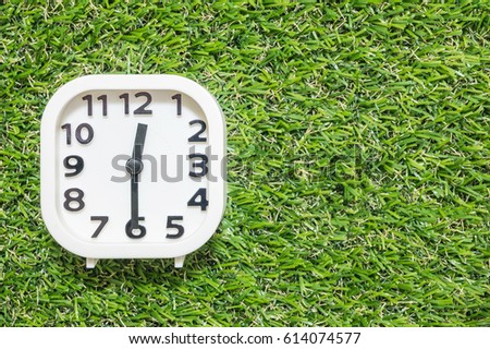 Closeup white clock for decorate show a half past twelve or 12:30 p.m. on green artificial grass floor textured background with copy space