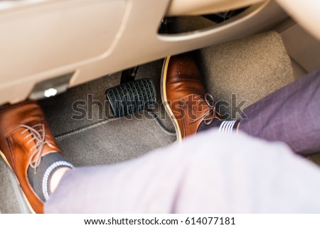 Closeup of a thirties man wearing brown shoes carrying a car accelerator and a brake / car safety system on the feet Accident and brake, danger of auto motor-driven bikes, driving habits Royalty-Free Stock Photo #614077181