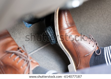 Closeup of a thirties man wearing brown shoes carrying a car accelerator and a brake / car safety system on the feet Accident and brake, danger of auto motor-driven bikes, driving habits Royalty-Free Stock Photo #614077187