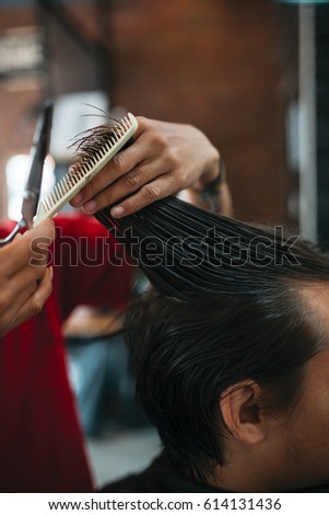 Close up of man that getting haircut by hairdresser with scissors and comb while sitting in chair. Barber shop