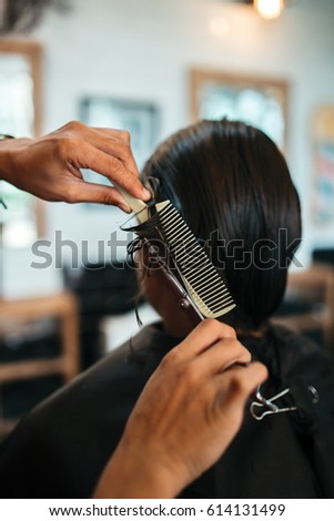 Close up of man that getting haircut by hairdresser with scissors and comb while sitting in chair. Back view in barber shop