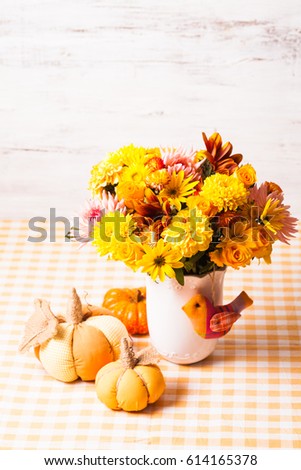 Vase with flowers and small orange textile pumpkins on a table
