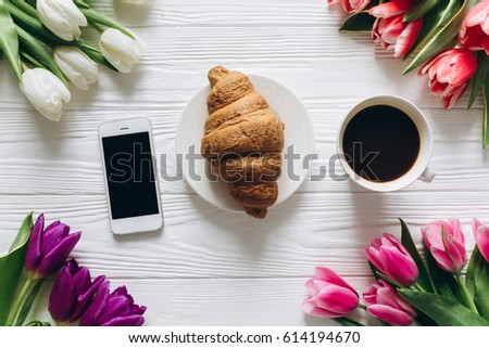 Cup of coffee with croissant and fresh tulips on a wooden background for Mother's Day