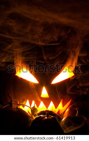 Jack-o-lantern with blazing and smoky eyes in smoke and small pumpkins