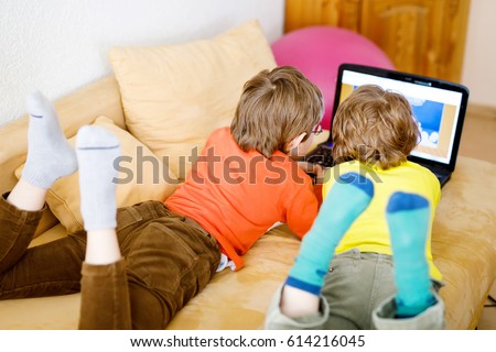 Happy little brothers, adorable kid boys watching television while lying. Funny children enjoying cartoons on notebook, laptop or computer. No faces of people