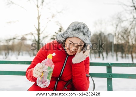 The girl walked in the park and has decided to have a rest, having sat down on a bench. She drinks water and laughs. Probably someone has very much made laugh her and she can't drink water in any way