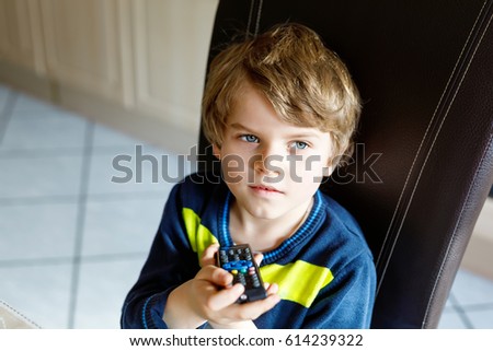 Cute little blond preschool kid boy watching tv. Happy child oprerating with remote control and choosing cartoons or education program. Television as not active leisure for children.