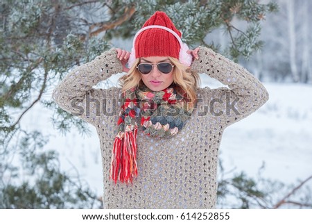 Beautiful girl in a red hat and sweater in the snow in pink with headphones