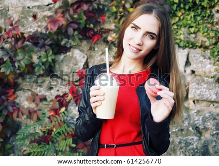 Outdoor closeup portrait of pretty stylish fashion girl having fun drinking chocolate milkshake with whipped cream and eating delicious macaroon. 