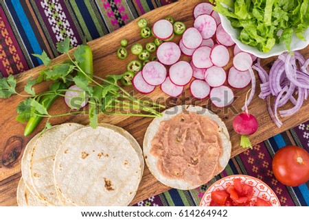 Top view of table with ingredients for vegetarian corn tacos -   refried beans, corn tortilla, radish, cut tomatoes.