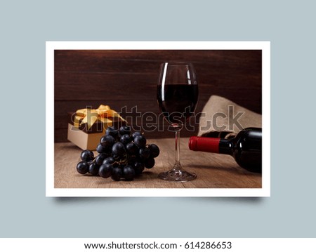 Red wine bottle. Wineglass with dark grapes branch. Gift boxes with bows on rustic wooden background. Photo frame design with shadow.