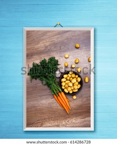 Potatoes in plate. Carrot, garlic and raw new potato. Fresh natural vegetables. Organic bio food on rustic wooden table. Photo frame on wooden rustic wall.