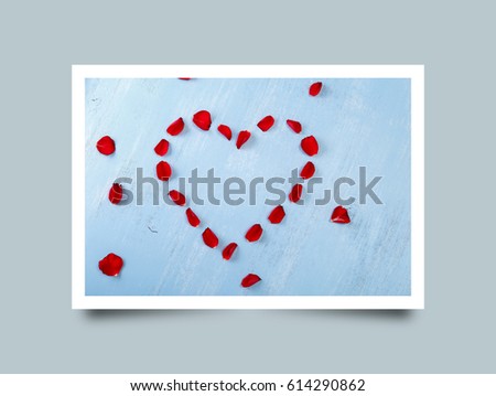 Heart of red rose petals on blue painted rustic background. Valentines day or love concept. Fresh natural flowers. Dirty grunge wooden board. Photo frame design with shadow.