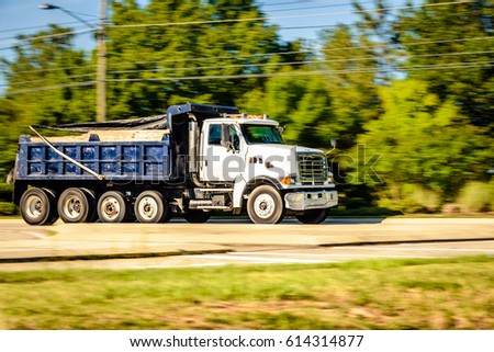 A dump truck is running down the highway captured early morning during summer season. This image was captured using panning technique to blur the background and emphasize motion.