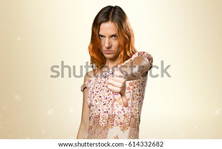 Pretty woman with orange hair making bad signal on ocher background