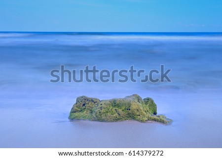 stones in a calm sea at sunset.green moss cover the rock,sea,Thailand.sea photographed daytime with long exposure.selective focus.