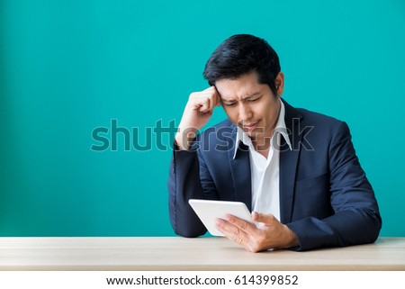 Businessman sitting at wood table and green wall and looking down at tablet computer screen at office,Feeling stress about financial crisis,stock market failure