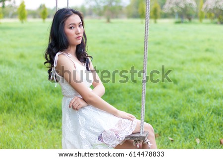 Portrait of Asian woman sitting on wood swing and grass field for background.