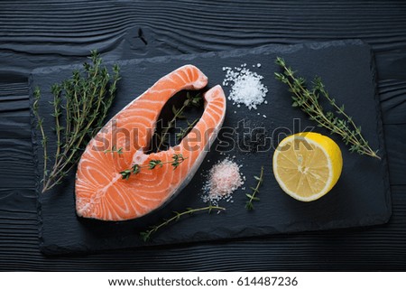 Stone slate with raw salmon steak, fresh thyme, lemon and various types of salt, high angle view
