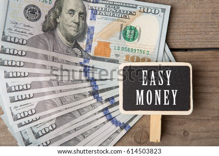 Finance concept - blackboard with text "easy money" and hundred dollar bills on wooden background