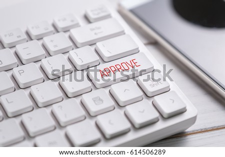 concept of to approve something, with message on enter key of white keyboard and red text on the wooden table and blurred mobile phone
